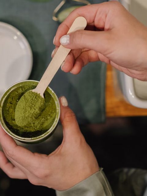A person scooping vibrant matcha powder into a cup, perfect for cozy culinary scenes.